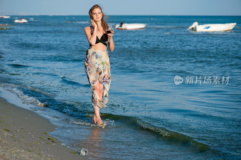 年轻女子在海滩上散步，手里拿着一个酒杯