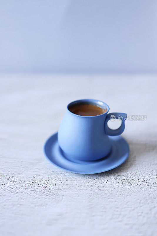 在浅灰色的混凝土地板上，用蓝色陶瓷杯盛着起泡的土耳其咖啡
