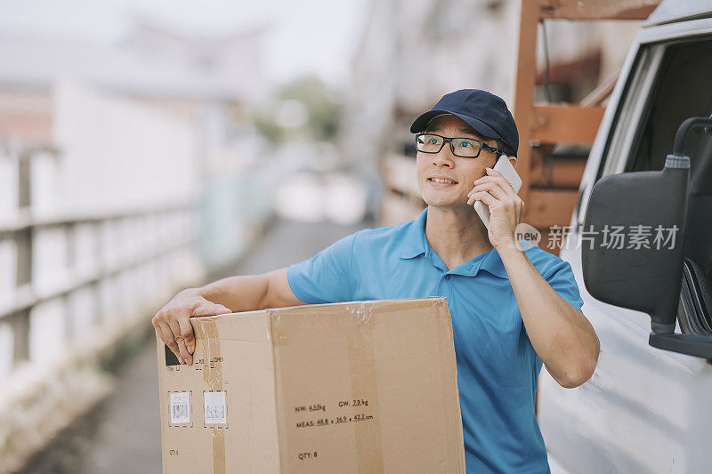 亚洲华人成熟男性送货员用电话呼叫客户旁边的小货车拿着纸箱