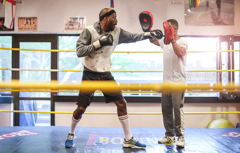 一名成年非洲男子与他的拳击教练在拳击场热身。