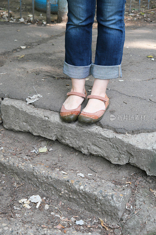 穿着牛仔裤和凉鞋的女性脚站在街道的台阶上