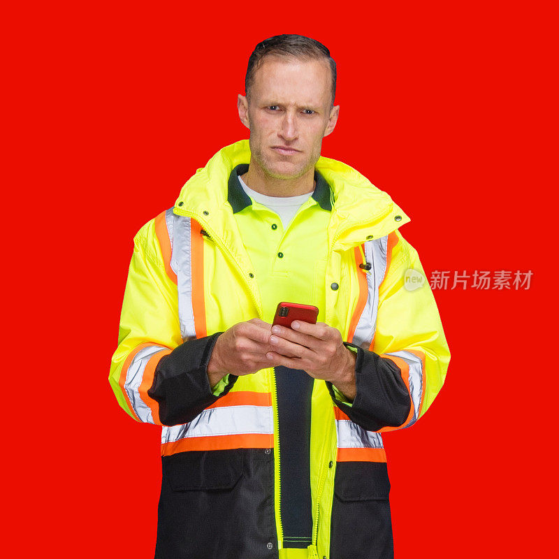 白人男性劳动者穿着马甲，用智能手机站在有色背景前面