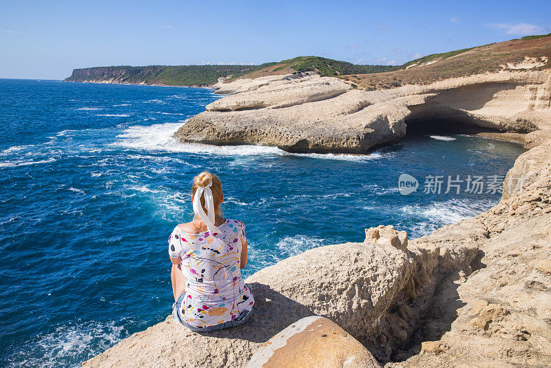 一个沉思的孤独女人坐在沙滩上，抱着膝盖，满怀希望地望着远方，撒丁岛，意大利。