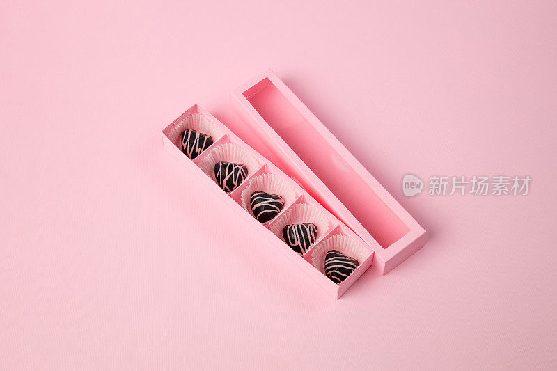 黑巧克力心形松露在一排打开倾斜的粉红盒子上