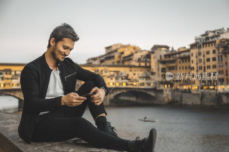 意大利佛罗伦萨托斯卡纳的一名年轻男子，面带微笑地看着智能手机，分享内容