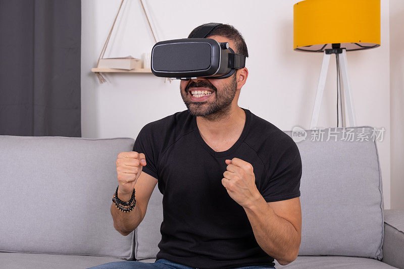 年轻人戴着VR头盔在家里的沙发上兴奋地打着手势，未来科技，教育视频游戏