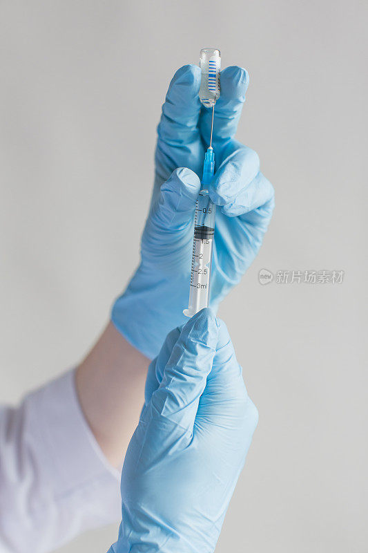 冠状病毒疫苗增效剂。注射器和针头。医生肖像在灰色背景的防护口罩和手套。穿着专业制服的医学专家。自信的护士。病毒流行