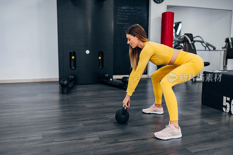 积极的女运动员带着壶铃在健身房锻炼。通过这种方式，它激活了身体的所有肌肉，并使它们绷紧。