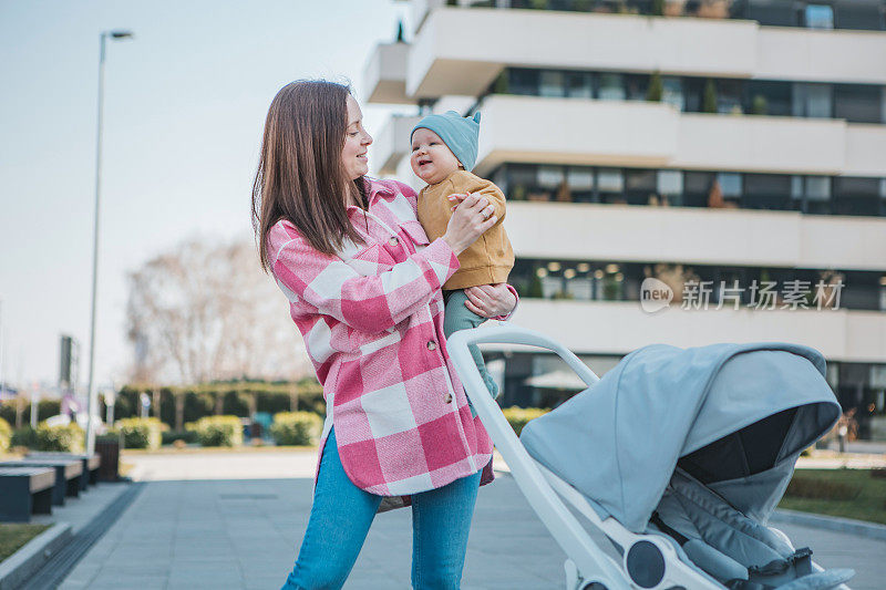 年轻的妈妈抱着婴儿，推着现代的婴儿车，漫步在城市中