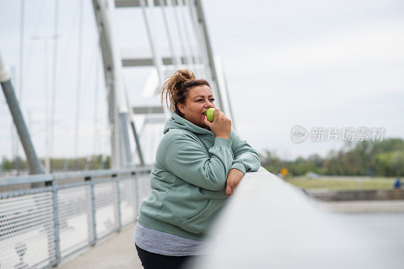 肥胖的拉丁妇女在精疲力尽的有氧减肥训练后吃着一个青苹果