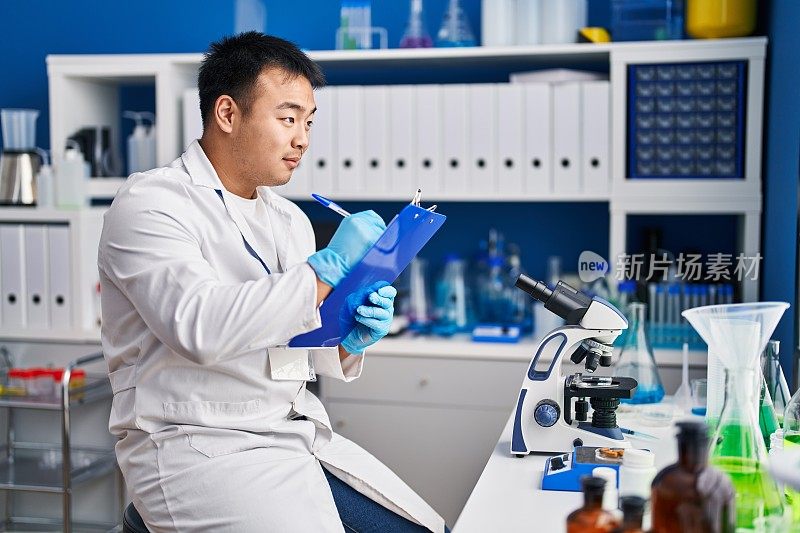 身穿科学家制服的中国青年在实验室的写字板上写字