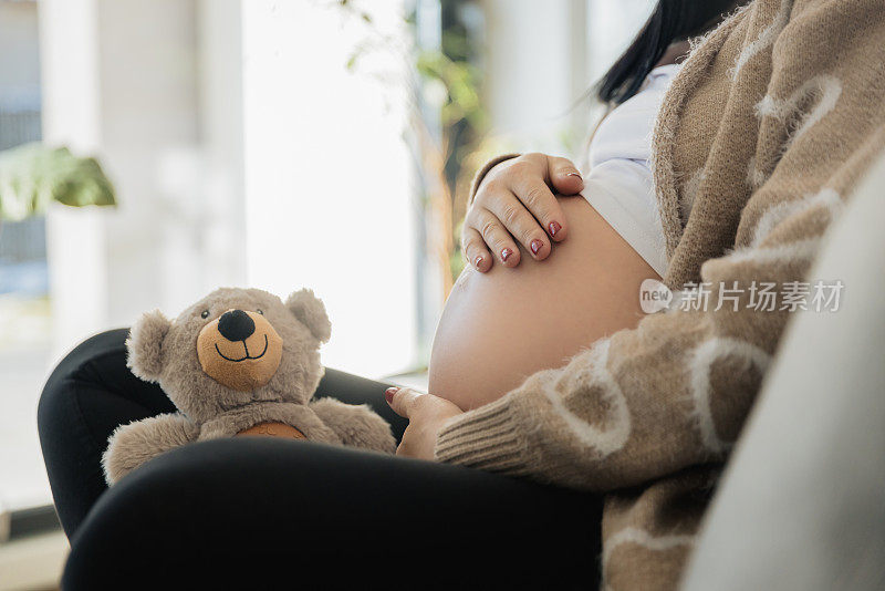 孕妇的腹部摸着她的肚子，泰迪熊坐在沙发上