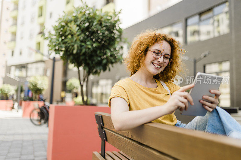 一个女人坐在长凳上看着平板电脑的照片