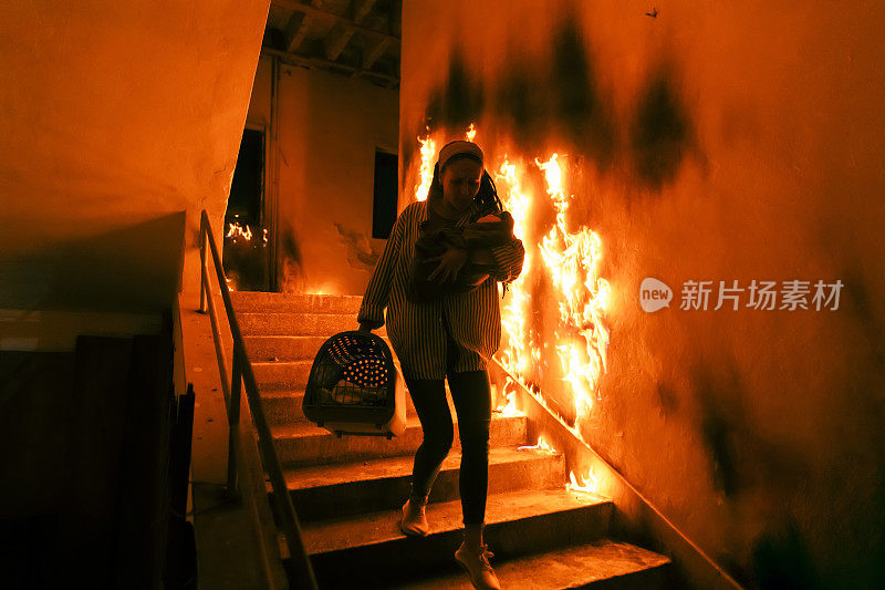 勇敢的消防员从着火的大楼里走下楼梯，将获救的女孩抱在怀里。明火，背景中有一名消防员。