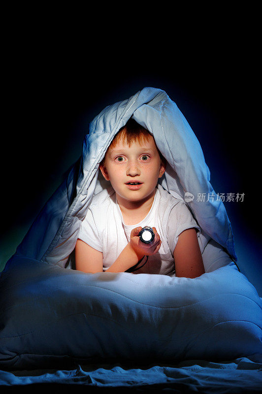 小男孩躲在毯子下拿着手电筒