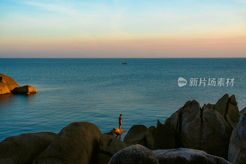 苏梅岛上，一名男子站在岩石上钓鱼