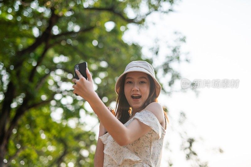 年轻的亚洲女子在公园里使用手机应用程序。美丽的女人在郁郁葱葱的绿色森林里查看手机上的应用程序