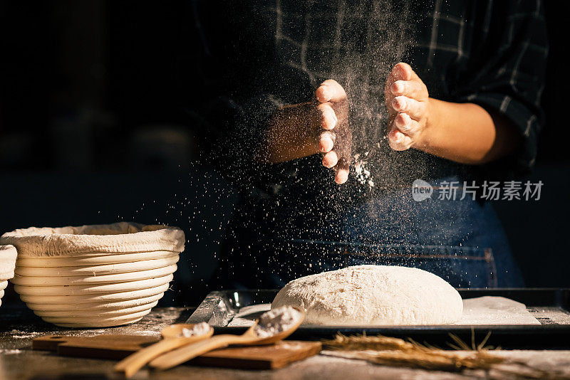 专业的面包师在厨房的桌子上制作酸面包或手工面包时，将面粉拍打在面团上。小生意在家自制面包店。