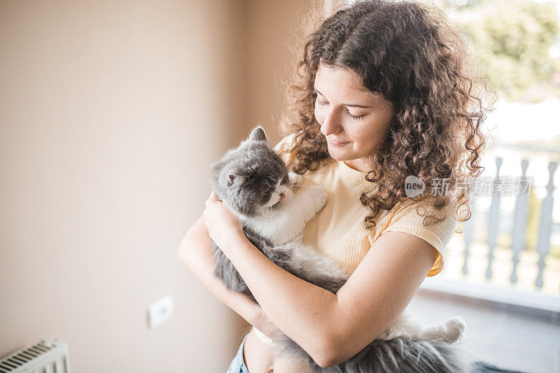 可爱的卷发女人手里抱着她那只灰白色的猫