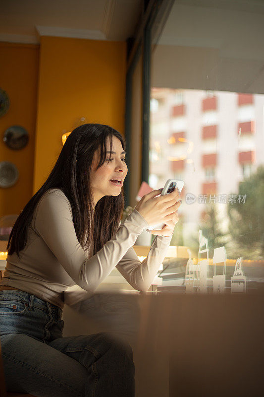 年轻女子坐在咖啡店里。她拿着她的手机。