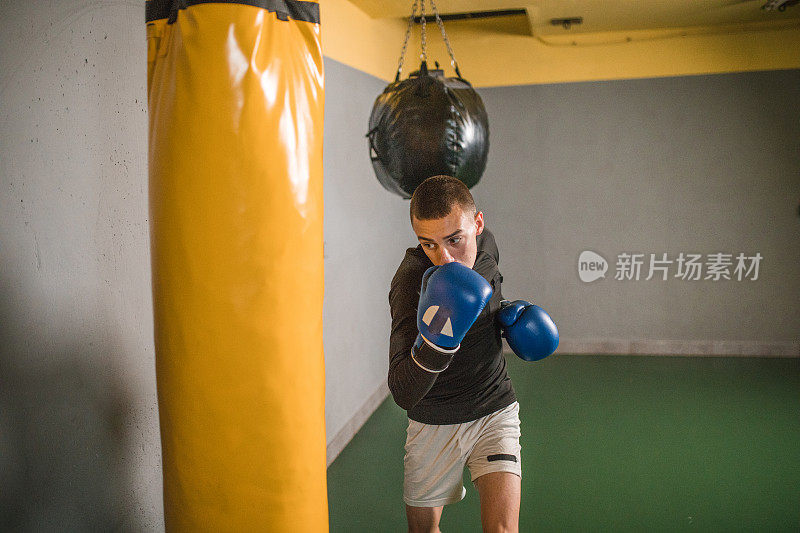 一名男拳击手在健身房里击打沙袋，锻炼肌肉