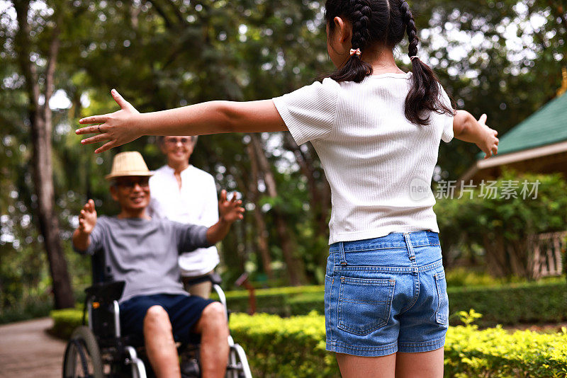 在公园里，孙女坐在轮椅上投入爷爷的怀抱，奶奶在一旁照顾