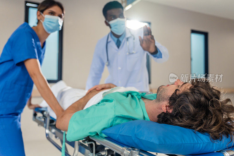 一群不同的医生在医院里移动重伤病人。有魅力的专业医护人员匆忙地将躺在担架上的急诊病人抬进手术室。