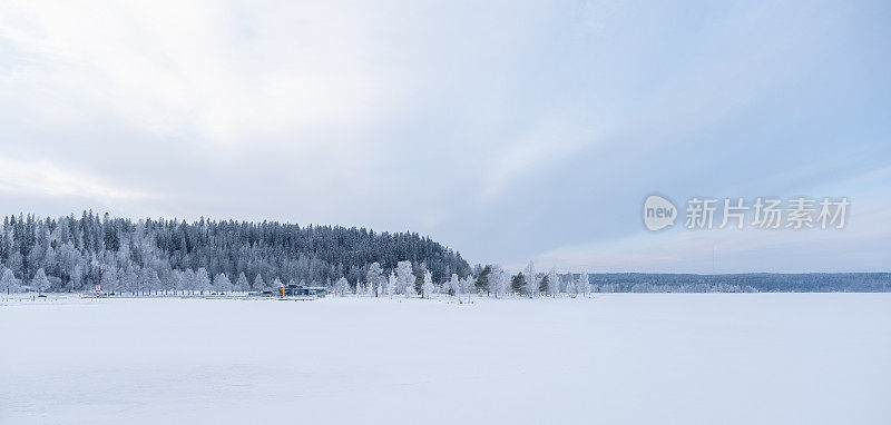 冬天的风景。冰雪覆盖的冰湖，在湖的岸边有一片白雪覆盖的森林。