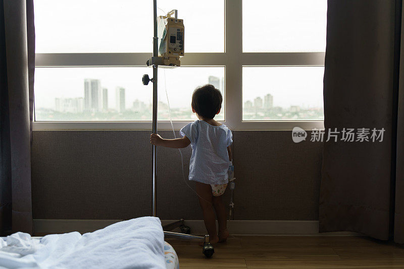 生病的小男孩站在医院的后视图，透过窗户向外看。