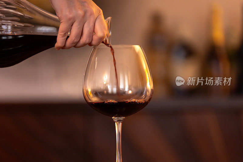 一个女人用手把酒瓶里的酒倒进酒杯。