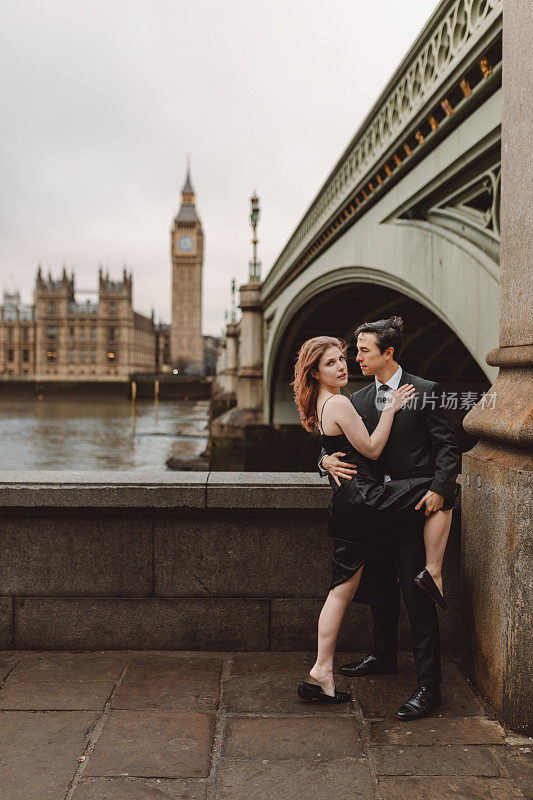 一对穿着黑色探戈的时髦年轻夫妇的肖像，在伦敦闪闪发光的天际线下，在图标的阴影中跳舞