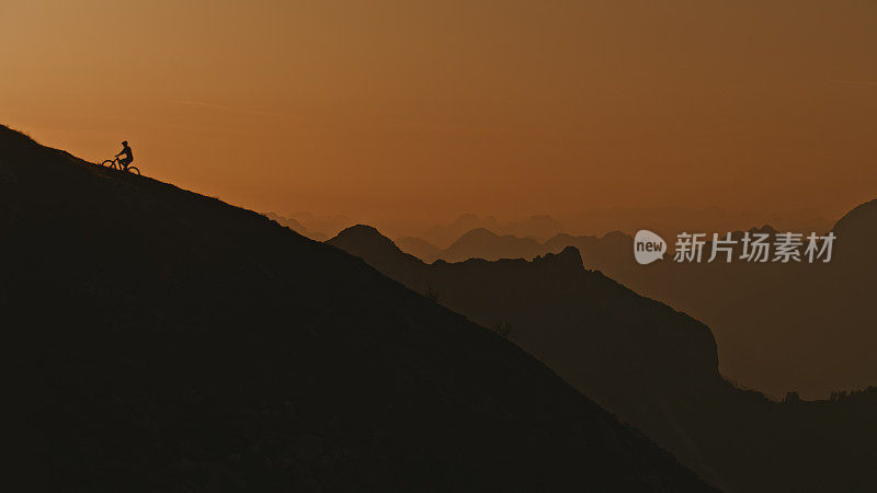 低角度远观山地自行车骑在山顶上对清澈的橙色天空在日落