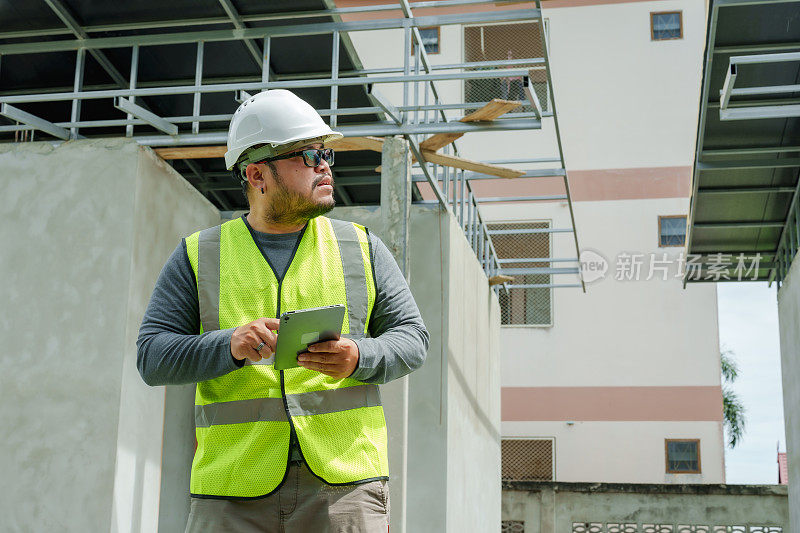 工程师经理领班年轻的亚洲工人建筑师设计师戴着白色安全帽在大楼外的平板上查看尚未完工的房屋工程的工作队列。