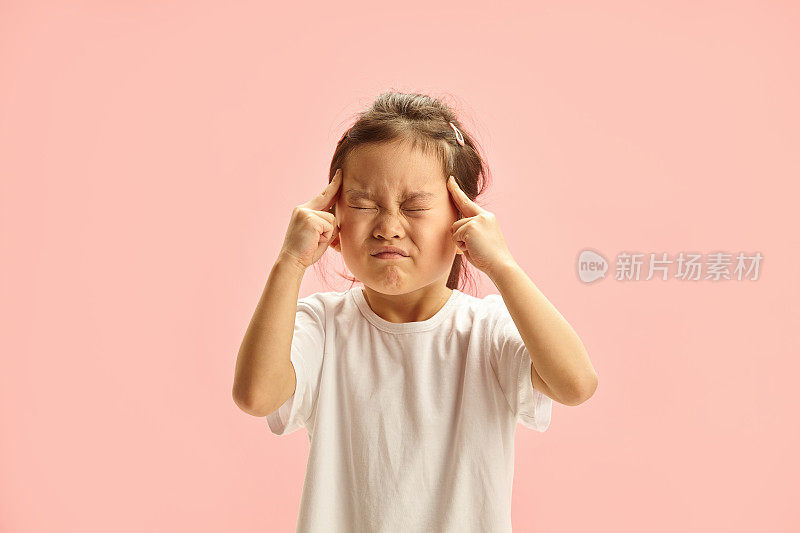 一个五岁的日本女孩闭着眼睛，手指放在太阳穴上，全神贯注地站在粉红色的地方