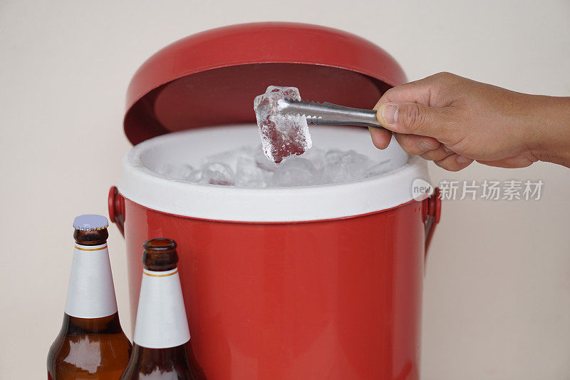 近距离用手抓住红色冰桶冷却器中的冰块来准备饮料。概念:将啤酒或酒精饮料或鸡尾酒与冰块混合，使其更有味道。