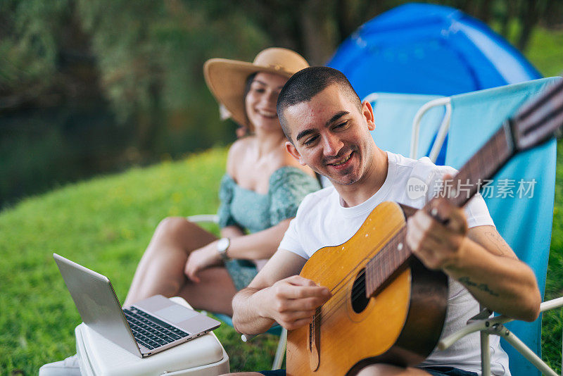 年轻的成年夫妇在大自然中放松，坐在他们的帐篷营地旁边。