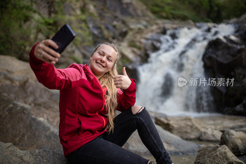 年轻的徒步旅行者在大自然中用手机自拍，背景是美丽的瀑布