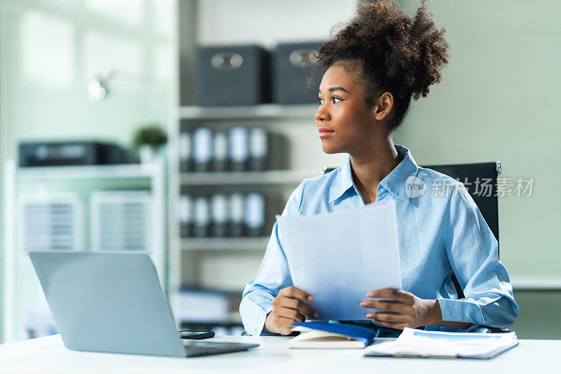 一位身穿蓝色正装衬衫、留着非洲式棕色头发的年轻非裔美国女性在一家现代化的办公室里做市场研究分析师，她正在分析商业图表A4。