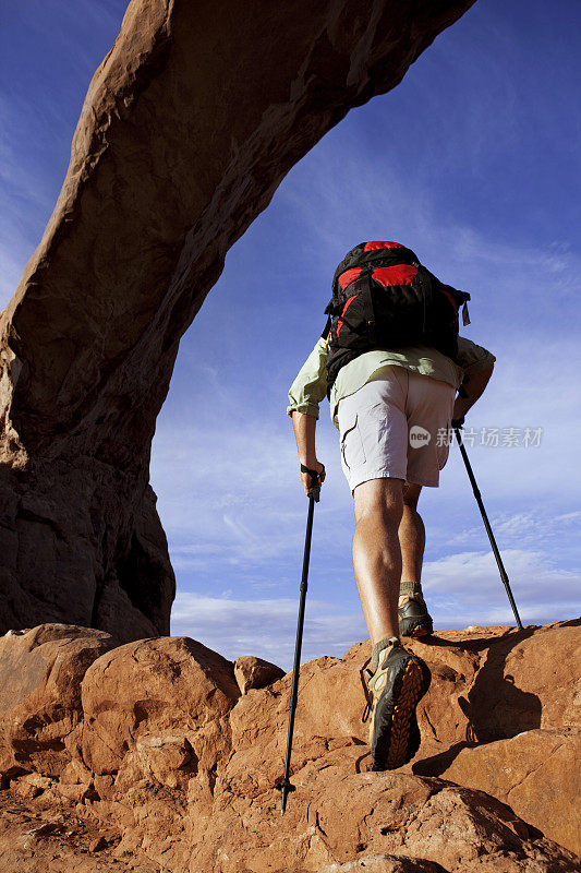 男性徒步者用攀登杆攀登陡峭的岩石