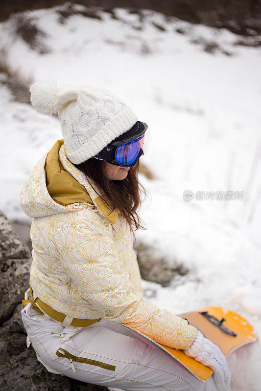 女人拿着滑雪板，背景是高山