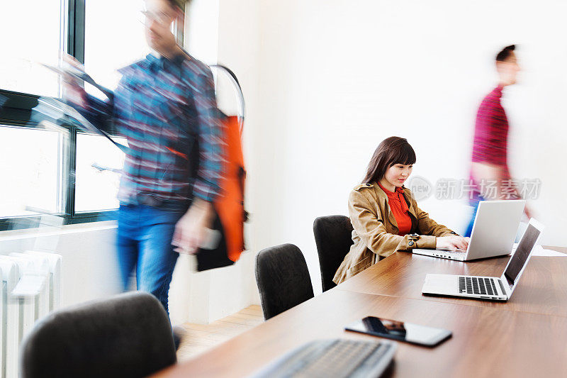 在繁忙的办公室里用笔记本电脑的年轻女商人