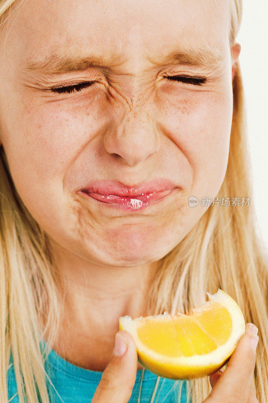 不高兴的金发小女孩尝了酸柠檬的味道做了个鬼脸