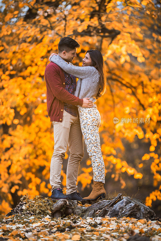 在秋天的公园里，一对年轻的情侣互相拥抱看着对方。