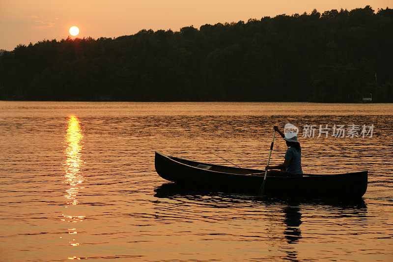 户外女孩在金色的夕阳中在湖中划着独木舟