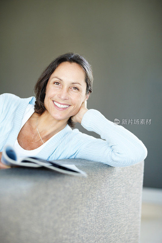 微笑着，成熟的女人拿着杂志在沙发上放松
