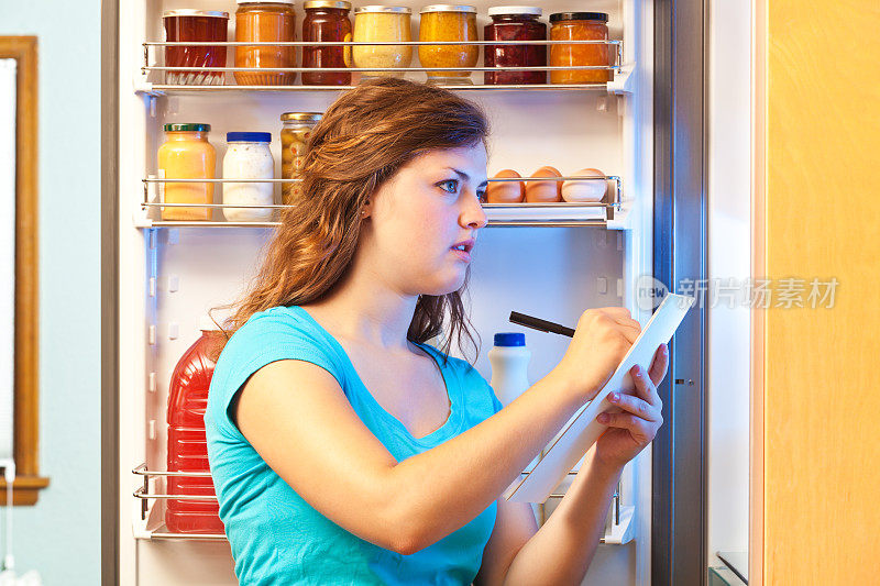 女人在冰箱前制作购物清单