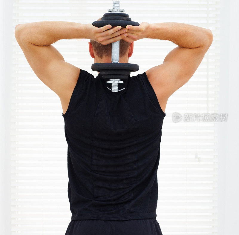 一个年轻人用哑铃锻炼他的三头肌的后视图