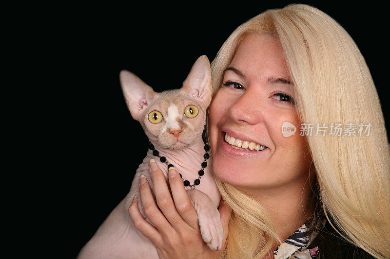 金发年轻女士抱着她的斯芬克斯猫对着镜头微笑