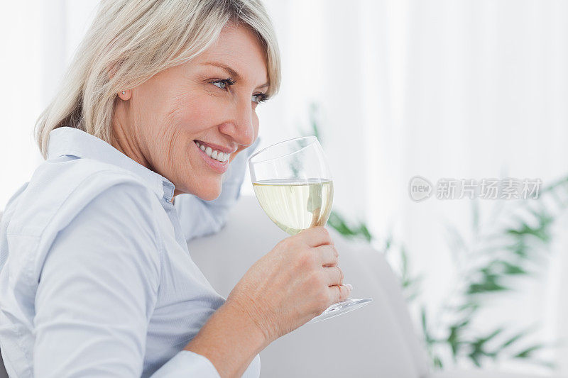 微笑的金发女人闻着她的白葡萄酒