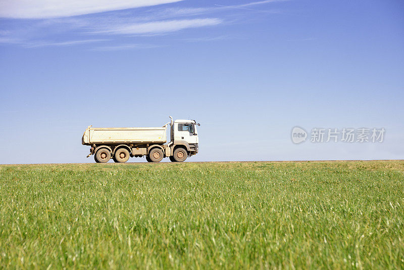 自卸卡车行驶在乡间小路上穿过田野